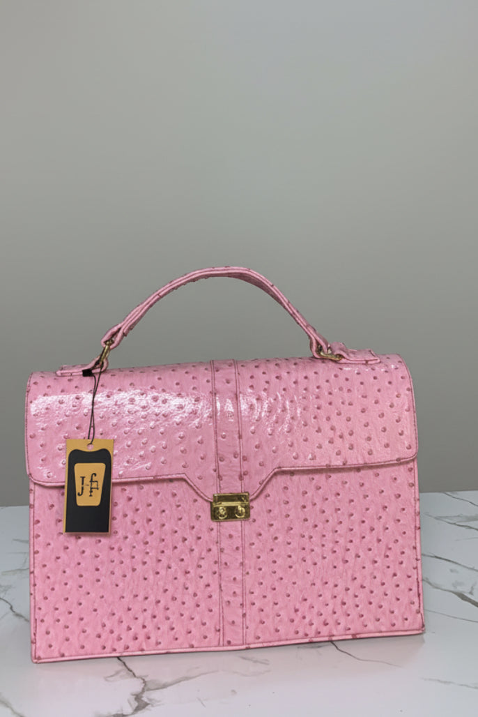 A pink ostrich-embossed leather handbag with gold hardware and a top handle, displayed on a marble surface in front of a branded 'Hazina Fits' sign.