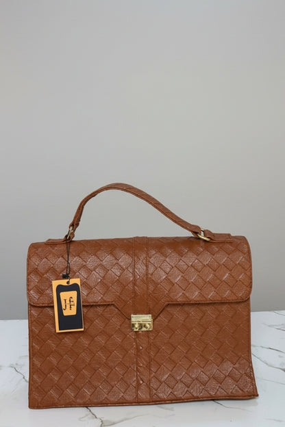 A brown woven leather handbag with a top handle and gold-tone clasp, displayed on a marble surface in front of a branded wall sign reading HAZINA FITS.