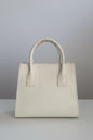A cream-colored ostrich leather handbag with double top handles, displayed on a white marble surface with a neutral indoor background.