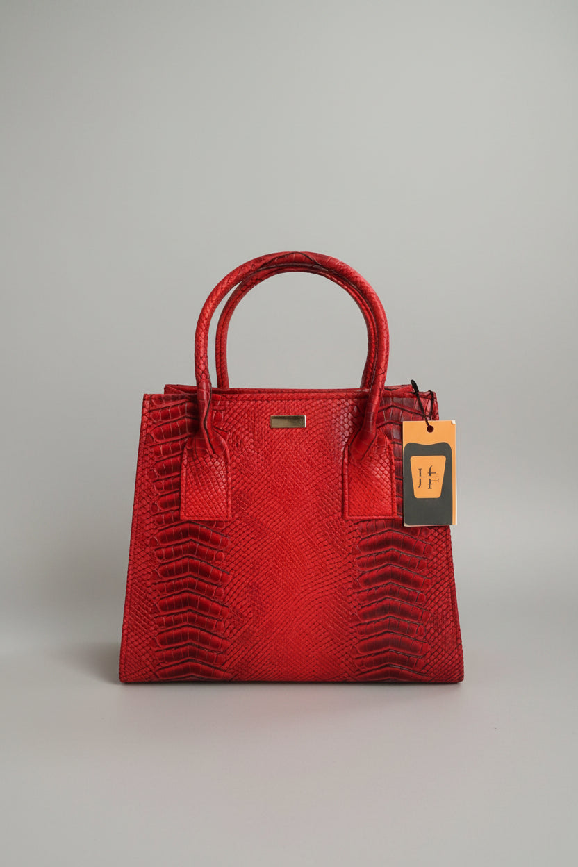 A bright red python-textured leather handbag with double top handles and a small gold-tone metal accent on the front, displayed on a marble surface with a hangtag attached.