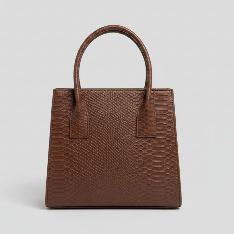 A brown textured handbag with a python-style embossed pattern, featuring two top handles and a structured rectangular shape, displayed on a marble surface.