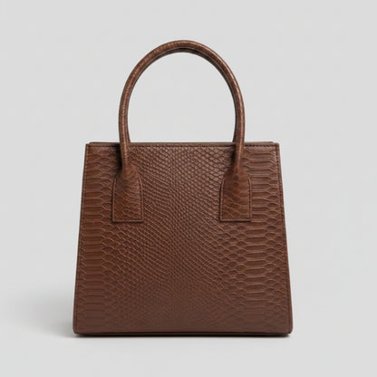 A brown textured handbag with a python-style embossed pattern, featuring two top handles and a structured rectangular shape, displayed on a marble surface.
