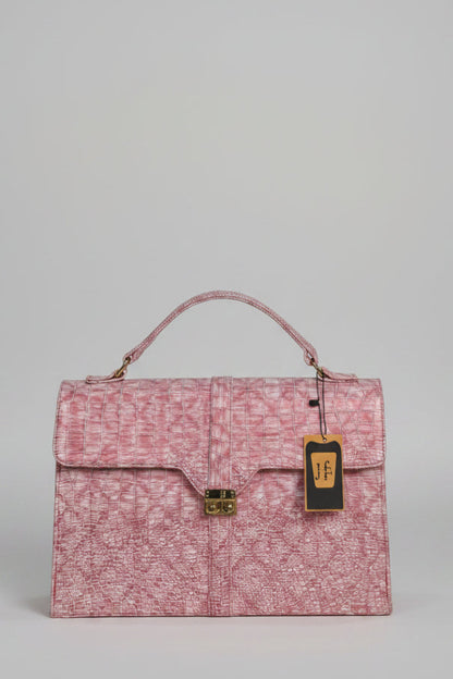A pink monogram-patterned handbag with a top handle and gold-tone clasp, displayed on a marble surface in front of a branded wall sign reading HAZINA FITS.