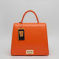 Bright orange textured leather handbag with a top handle, hanging tag, and gold-tone front clasp, displayed on a marble surface.
